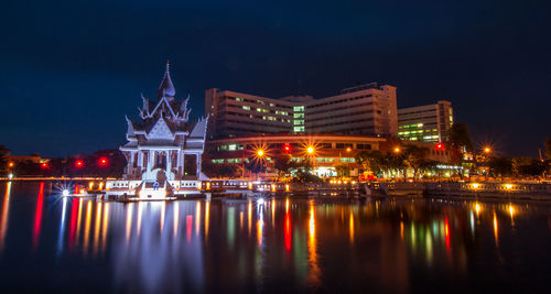 Illuminated buildings by river against sky at night