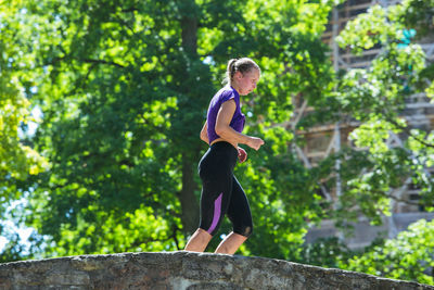 Side view of woman with arms outstretched against trees