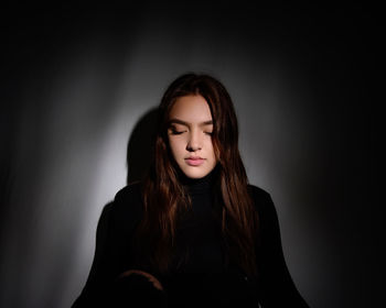 Beautiful young woman sitting against wall in darkroom