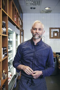 Portrait of mature salesman standing by rack in deli