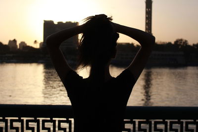Rear view of silhouette woman with hands in hair standing against sky