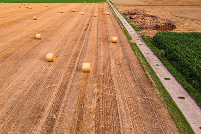 A field with hay bales and a dirt road that extends to the horizon from above aerial shot