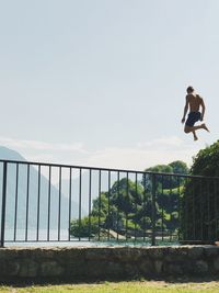 Man on railing by bridge against sky