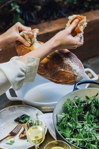 Woman breaking bread at summer evening dinner table with salad, white wine, steamed mussels