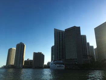 Modern buildings by river against clear sky