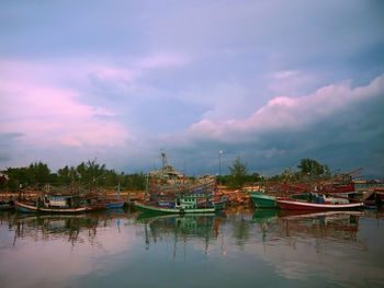 Boats moored at harbor on lake against cloudy sky