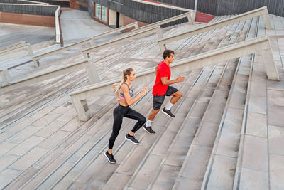 From above side view of couple of runners in sportswear jogging on staircase while working out in town