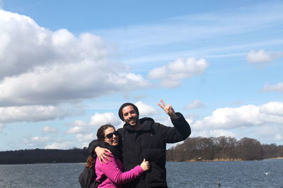 Portrait of couple standing by lake against cloudy sky