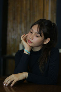 Young woman looking down while sitting on table