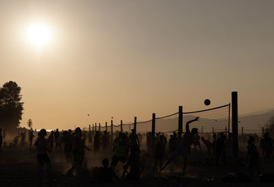 Silhouette people playing volleyball at beach during sunset