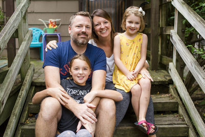 Portrait of happy family sitting on steps against house in yard
