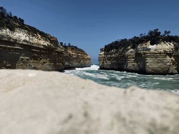 Rock formations by sea against clear blue sky