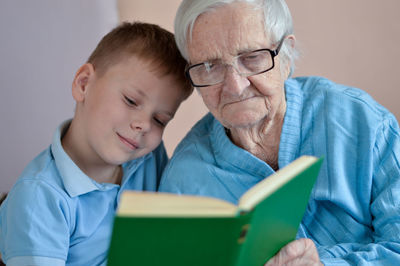 Portrait of white-hair eldery woman 90 years old with great-grandson at home, reading book together