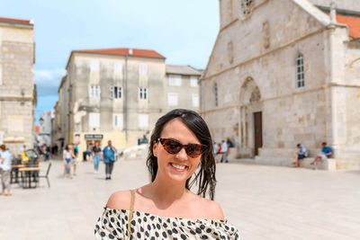 Portrait of happy young woman standing in square in old town.