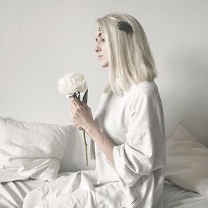 Young woman holding flower while sitting on bed at home