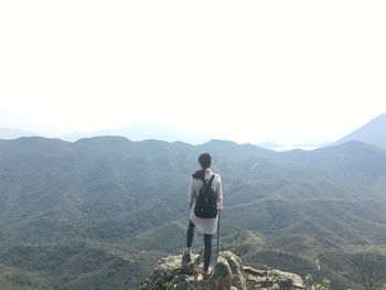 Full length rear view of hiker standing on cliff by mountains against sky