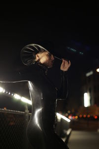 Side view of young woman looking at illuminated camera at night