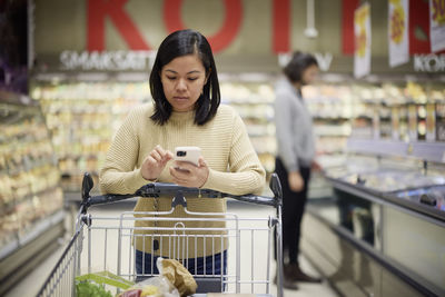 Woman doing shopping in supermarket and using cell phone to compare prices or checking shopping list