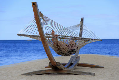 Woman relaxing in hammock at beach against sky