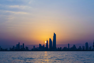 Sea with buildings in background at sunset