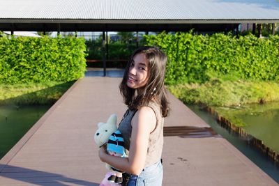 Portrait of smiling woman holding stuffed toy while standing outdoors