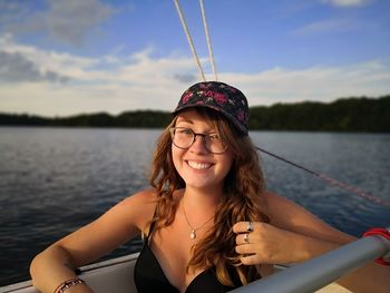Portrait of smiling young woman wearing eyeglasses and hat in boat against sky