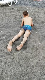 A boy in beach trunks lies on a rocky beach by the sea