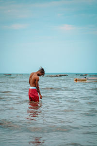 Full length of shirtless man in sea against sky