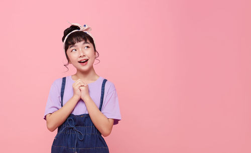 Portrait of smiling girl standing against pink background