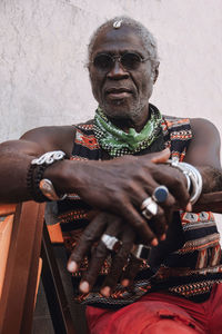 Cool middle aged african american male in rings and modern sunglasses sitting on chair in daylight