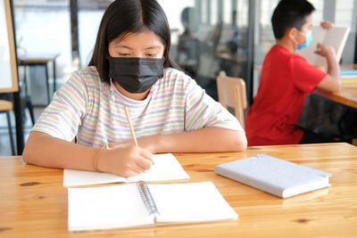 Asian girl student wearing face mask studying writing notes doing homework in library. learning e