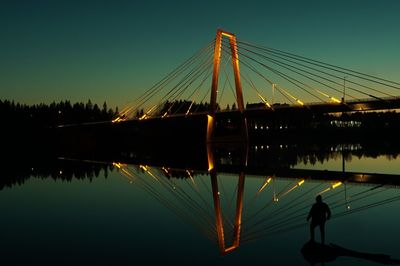 Silhouette bridge over river against sky at dusk