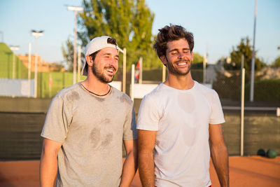 Smiling male friends standing on field during sunny day