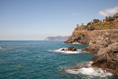 Distant view of people enjoying on rocks by sea against clear sky