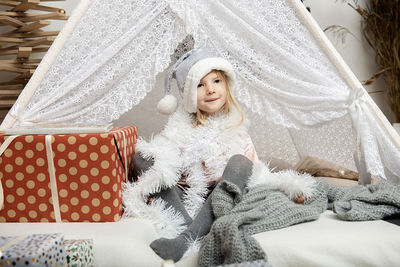 Portrait of a  little girl child wearing a silver color christmas hat sitting between gift boxes.