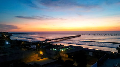 High angle view of illuminated city by sea against sky during sunset