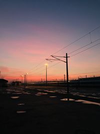 Silhouette electricity pylon by road against romantic sky at sunset