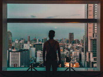 Rear view of man standing by cityscape against sky