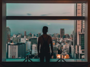 Rear view of man standing by window against cityscape