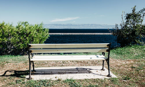 Empty bench in park by sea against sky