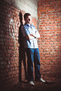 Full length of young man standing against brick wall