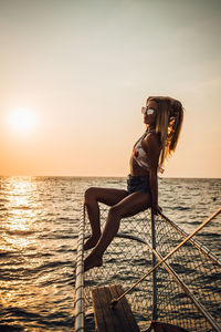 Woman with umbrella on sea against sky during sunset