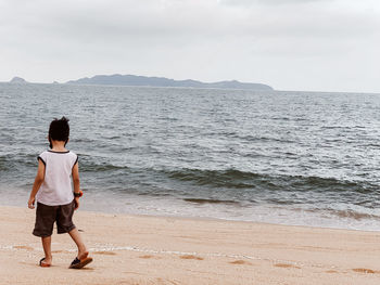 Rear view of boy standing on beach against sky