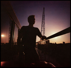 Silhouette man standing by illuminated city against sky at sunset