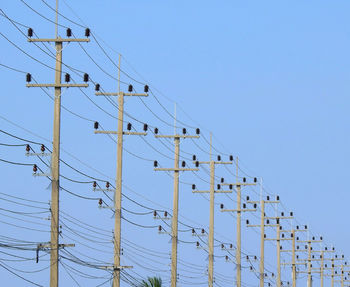 Low angle view of power lines in row against clear blue sky