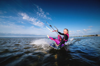 A young caucasian woman in a wetsuit rides a kiteboard. an athlete performs a trick while sitting on