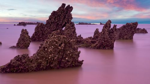 Rock formation in sea against sky during sunset