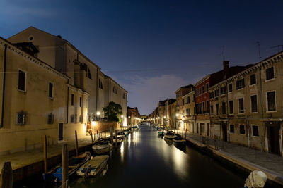 Boats moored on canal amidst buildings at night