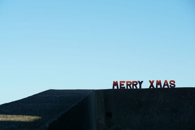 Low angle view of text on wall against clear blue sky