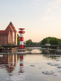 Buildings by lake against sky during sunset